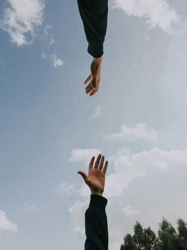Two hands reaching toward each other across a soft sky